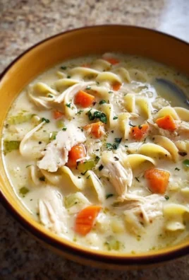 Delicious creamy chicken noodle soup in a bowl with ingredients around it