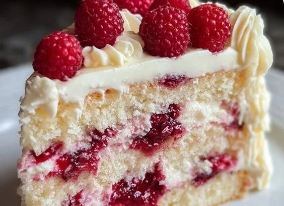 Delicious White Chocolate Raspberry Cake decorated with fresh raspberries and white chocolate shavings.